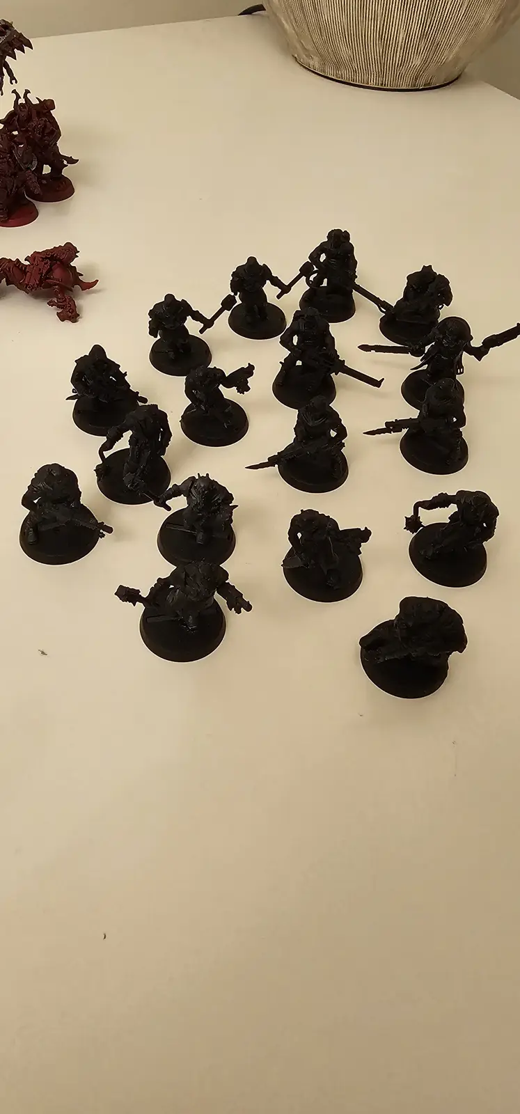 A collection of unpainted black miniature figurines, likely for a tabletop wargame, are arranged on a white surface. Some…