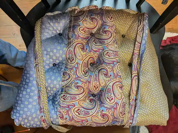 A shirt with multiple conflicting patterns — paisley, geometric squares, and small floral motifs — is draped over a black…